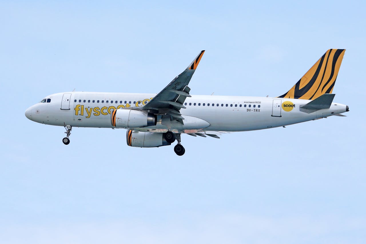 Airbus A320 flying high with Scoot Airlines branding against a clear blue sky.