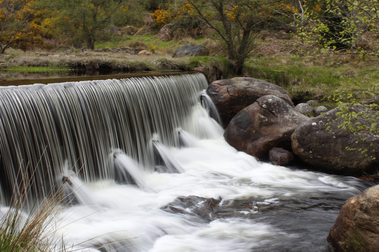 A serene forest waterfall with smooth, flowing water cascading over rocks, surrounded by lush greenery.