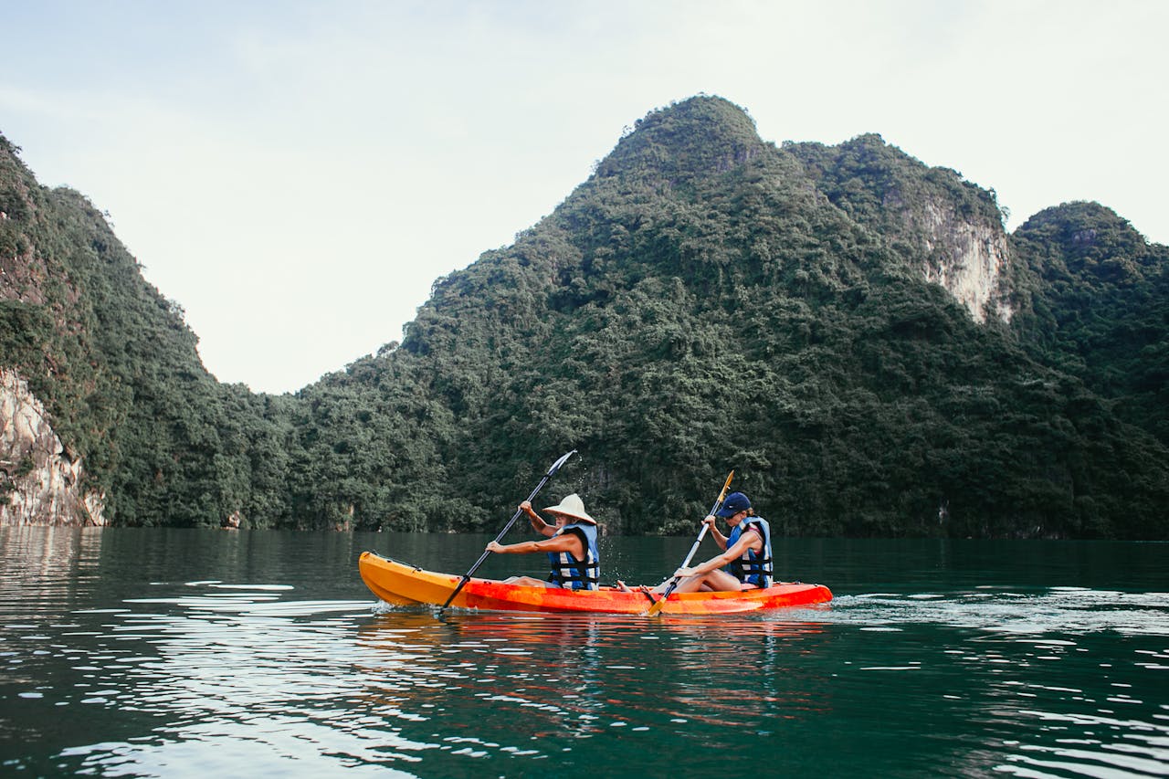 Two people kayaking on a serene mountain lake surrounded by lush green hills.